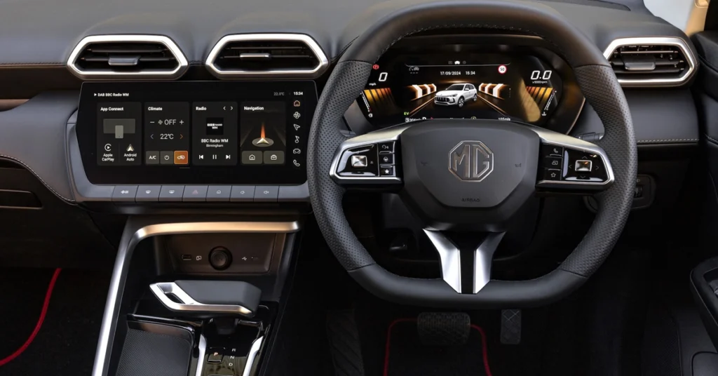 Close-up shot of the interior of a MG MG ZS Hybrid+ SUV, focusing on the dashboard and steering wheel. The dashboard features a large touchscreen display on the left, showing various car functions and settings. 