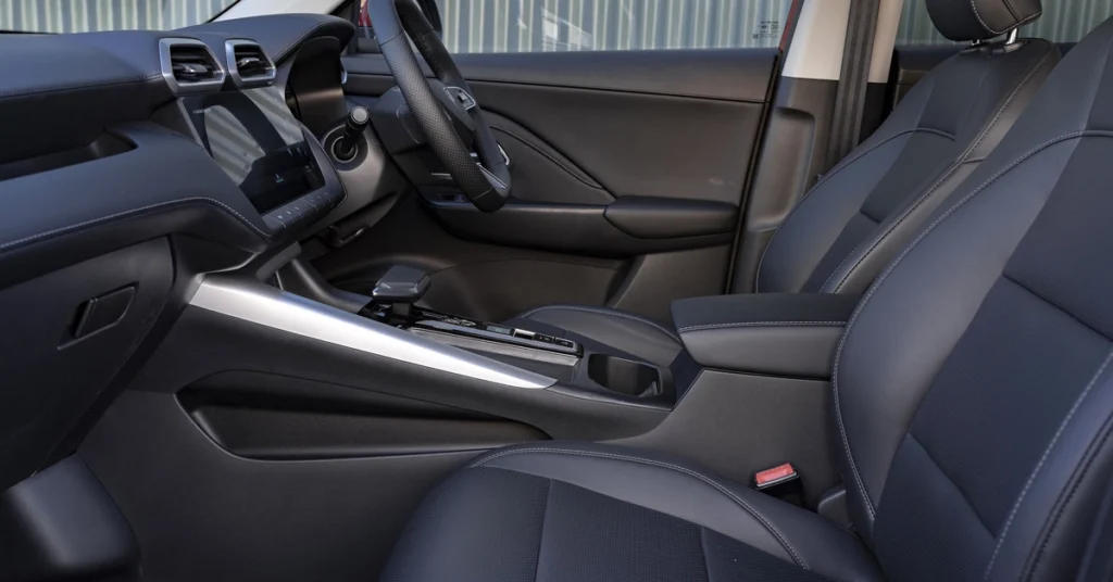 A detailed shot of the interior of a MG MG ZS Hybrid+ SUV, focusing on the driver's side. The seats are upholstered in a dark, possibly black or very dark gray, material with lighter stitching. 
