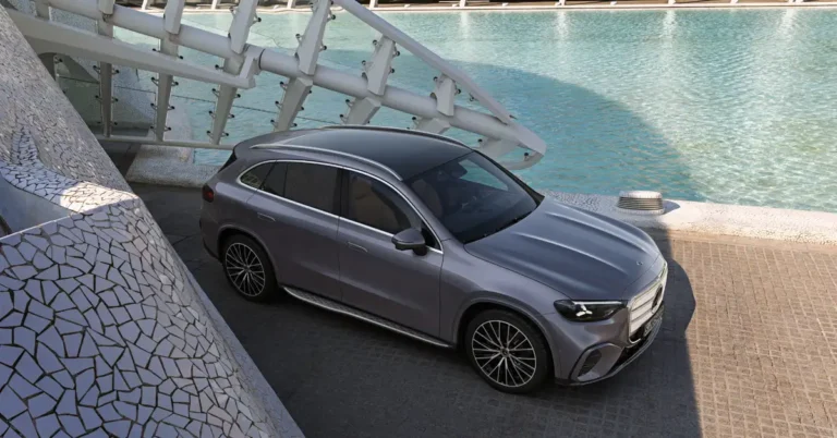 A gray Mercedes-Benz GLC SUV is parked on a paved surface next to a structure covered in white mosaic tiles, with a light blue pool of water and a white architectural structure in the background, captured in a well-lit, high-resolution photograph.