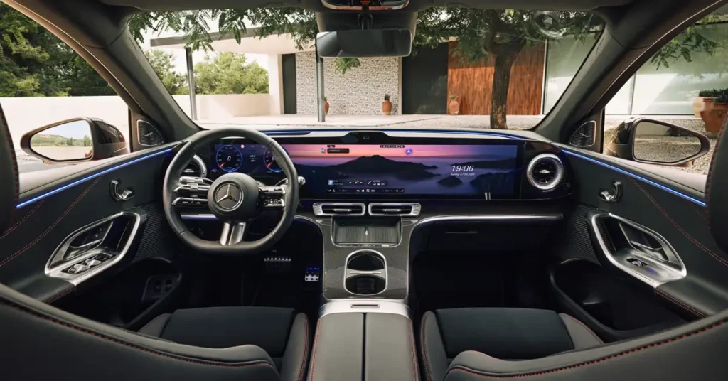 Interior view of a Mercedes-Benz GLC EV 2026car, showcasing a modern dashboard with a large, integrated display screen showing a landscape at sunset, digital instrument cluster, and sleek design elements, the seats are black with red stitching, the exterior view through the windshield reveals a house with trees.