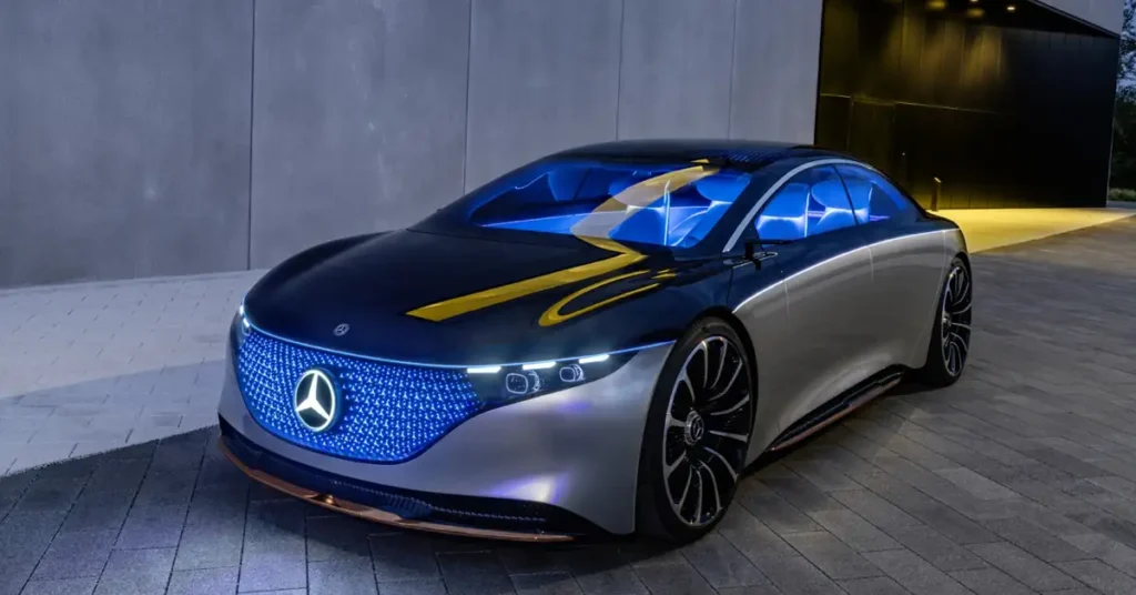 A Mercedes-Benz Vision EQS: The Electric Luxury Saloon Shaping the Future of Sustainable Driving two-tone Mercedes-Benz concept car with a black top and silver bottom, featuring a glowing blue grill with the Mercedes logo, blue-tinted windows, and intricate black and silver rims, parked on a paved surface in front of a modern building with a dark entrance