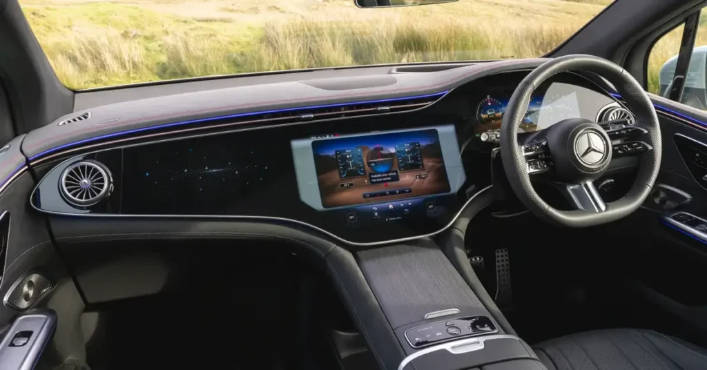 Interior of a Mercedes-Benz EQE SUV , featuring a black dashboard with a large digital display screen, a steering wheel with the Mercedes-Benz logo, and air vents with a turbine-like design.
