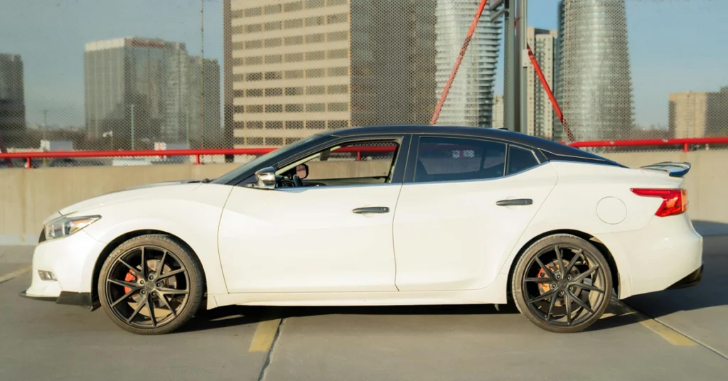 A side view captures a white Nissan Maxima with a black roof, parked on a concrete surface marked with yellow lines.