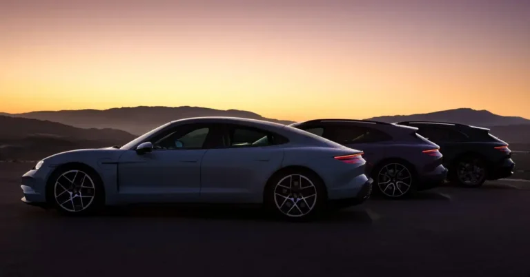 Three Porsche Taycan cars are parked in a row against a backdrop of mountains and a sunset sky. The first car is a light blue color, the second is a dark blue, and the third is black.