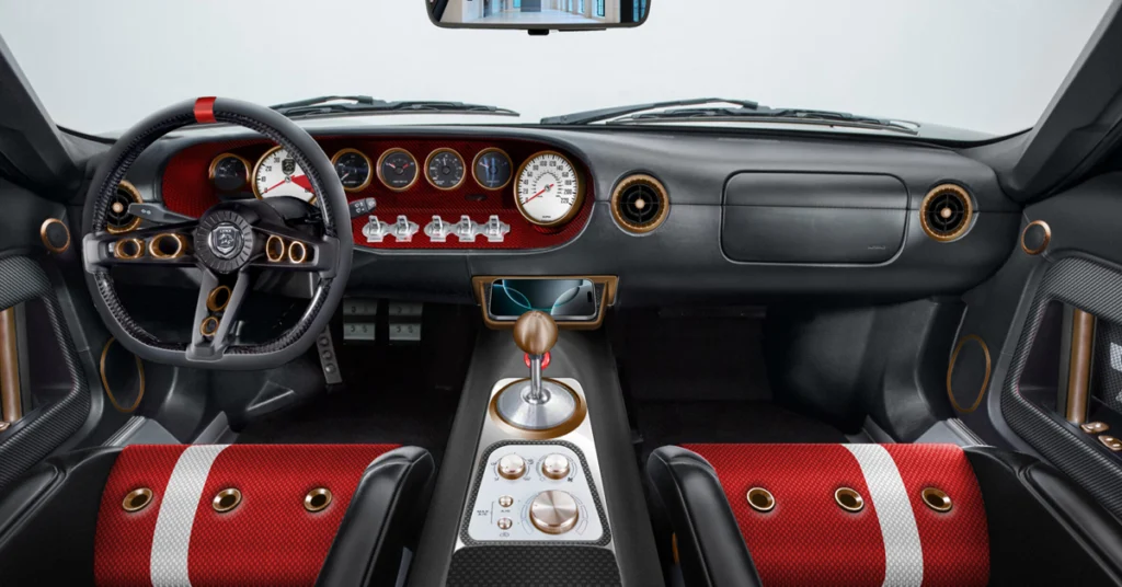 A detailed view of a Ford Lynx GT1car's interior, focusing on the dashboard, steering wheel, and center console. The dashboard is a combination of black and red, with several circular gauges trimmed in gold.