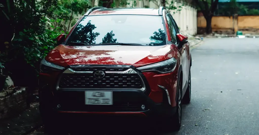 A front-facing shot of a red Toyota SUV parked on a street, with greenery visible on the left side of the frame.