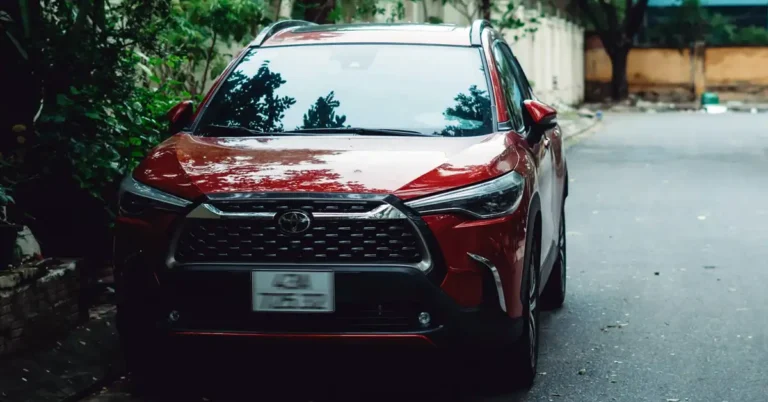 A front-facing shot of a red Toyota SUV parked on a street, with greenery visible on the left side of the frame.
