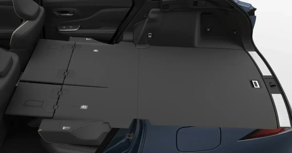A high-angle, medium shot depicts the interior of a Toyota Crown Estate 2025 trunk, showcasing a dark gray, flat, and foldable trunk floor. The floor is divided into sections, with visible hinges and latches indicating its foldable nature.