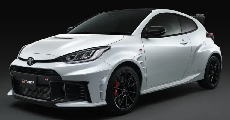 A white Toyota GR Yaris with a black roof and black wheels is parked in front of a black background. The car is a three-door hatchback with a sporty design. It has a large front grille, a hood scoop, and a rear spoiler.
