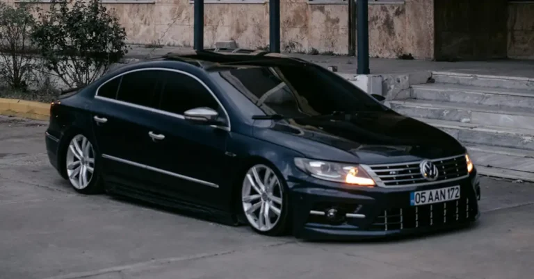 A sleek, dark blue Volkswagen Volkswagen Passat is parked on a paved surface, with a building in the background. The car is heavily modified, featuring a lowered suspension and custom silver wheels.