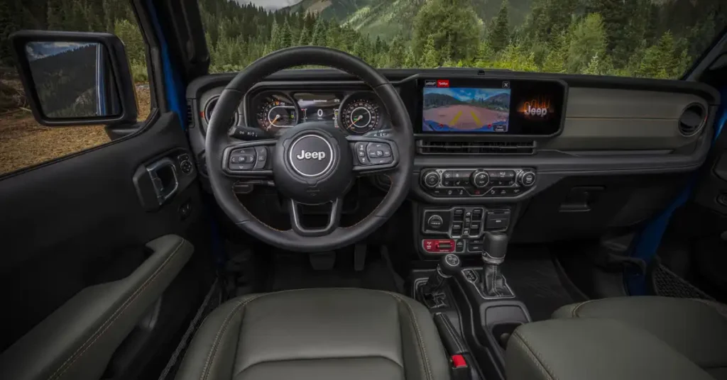 The image shows the interior of a 2025 Jeep Gladiator, viewed from the passenger seat. The dashboard is dominated by a large, black steering wheel with the Jeep logo in the center.