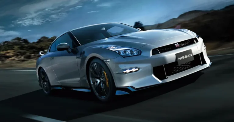 A silver 2025 Nissan GT-R  is captured in motion on a dark asphalt road, with a backdrop of blurred trees and a cloudy sky. The car's sleek design is accentuated by its aerodynamic features, including a rear spoiler and aggressive front fascia.