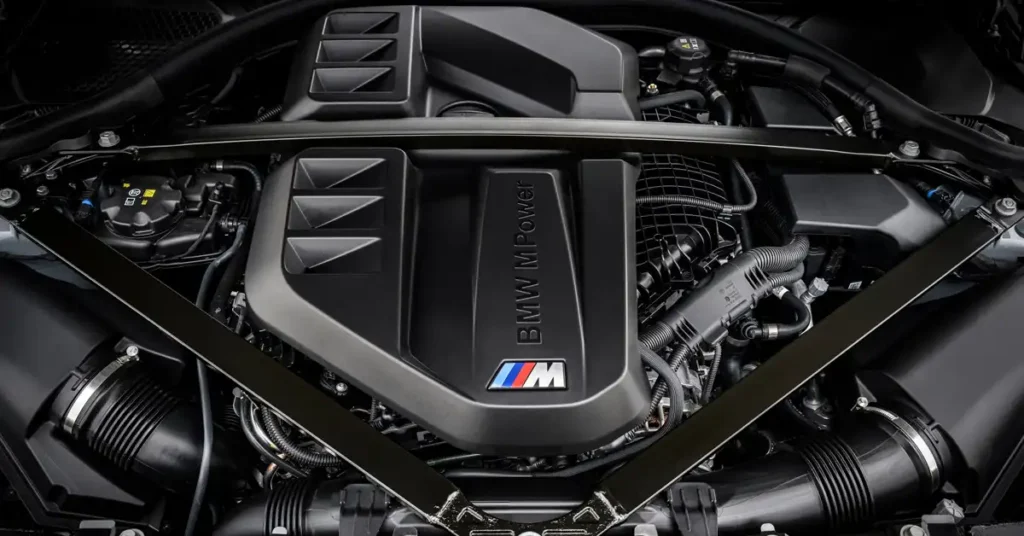 A close-up, high-angle shot shows the engine of a BMW M2 CS car. The engine is predominantly black with some silver accents.