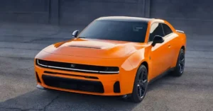A vibrant orange 2026 Dodge Charger , the car features a sleek black roof that contrasts sharply with its bright body. The wheels are a matching black, complementing the roof and adding to the car's aggressive stance.