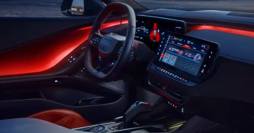 Interior of a 2025 Dodge Charge with a black steering wheel with the word "DODGE" in the center, a large digital display in the center console, and red ambient lighting along the dashboard and door panels. T