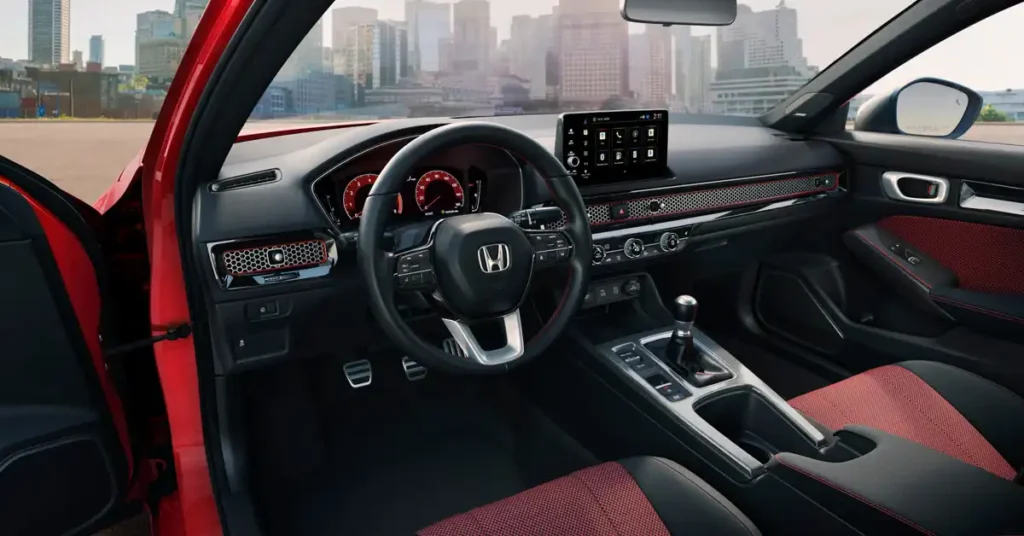 The image shows the interior of a red 2026 Honda Civic Si, specifically the driver's side. The car's interior is black with red accents. The dashboard features a digital instrument cluster and a central touchscreen infotainment system.