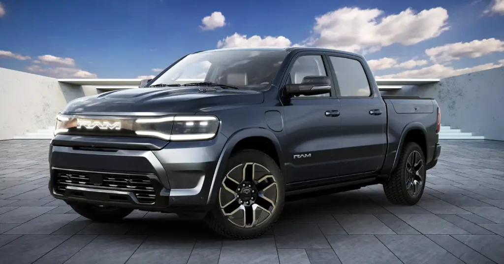 A digital photo of a dark gray 2026 Ram 1500 REV pickup truck is set against a backdrop of a blue sky with scattered clouds and a modern architectural structure. The truck is the primary focus, positioned at a slight angle to the viewer, showcasing its front and side profile. The front of the truck features a prominent, illuminated "RAM" logo across the grille, flanked by sleek, modern headlights.