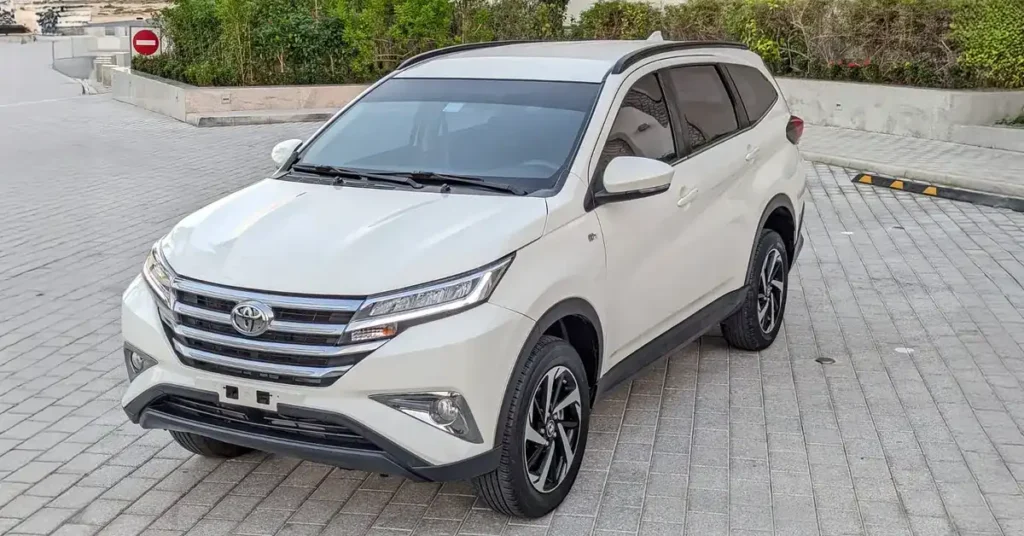 A white Toyota Rush SUV is parked on a paved surface. The car is facing the left side of the frame, with its front end slightly angled towards the viewer.