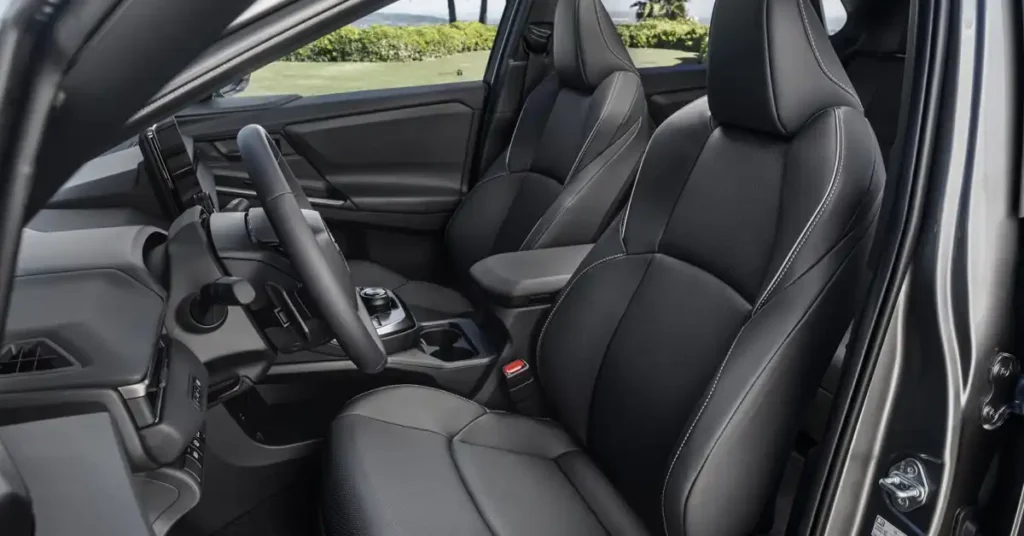 A close-up, eye-level shot shows the interior of a 2025 Toyota bZ4X SUV, focusing on the front passenger and driver seats. The seats are upholstered in black leather with white stitching, and the passenger seat is closer to the camera, angled slightly to the right.