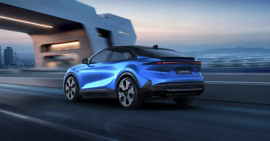 A sleek, blue 2026 Alpine A390 car is captured in motion from a rear three-quarter view, driving on a highway. The car's design is modern and aerodynamic, with sharp lines and a black roof. In the background, a blurred cityscape with tall buildings and a distinctive architectural structure with illuminated elements suggests an urban environment.