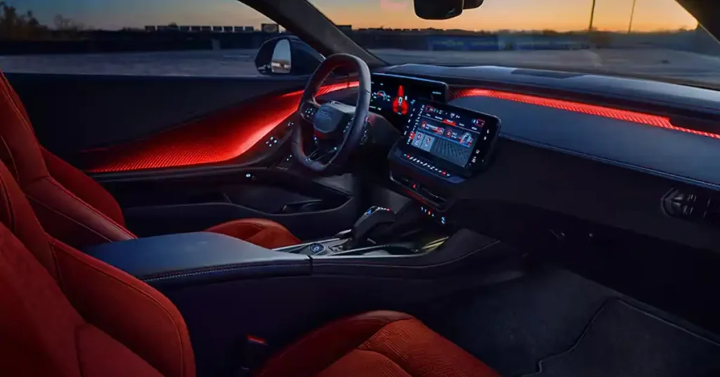 The image shows the interior of a 2026 Dodge Charger Daytona sports car, with a focus on the driver's side. The seats are upholstered in a vibrant red material with a textured pattern. The dashboard features a large, central touchscreen display and a digital instrument cluster behind the steering wheel.