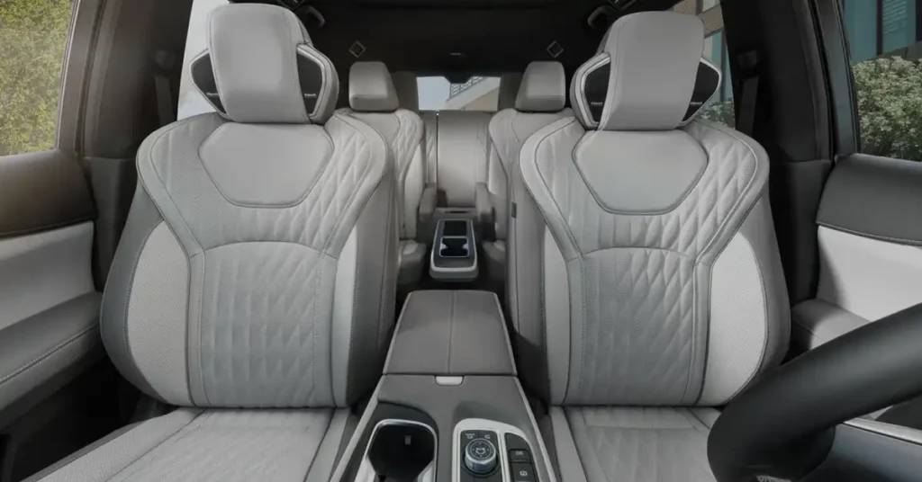 A wide-angle shot captures the luxurious interior of a 2026 INFINITI QX60 SUV, focusing on the front and second rows of seats. The seats are upholstered in a sophisticated light gray leather with intricate diamond-pattern stitching on the backrests and seat cushions, contrasted by darker gray accents on the sides.
