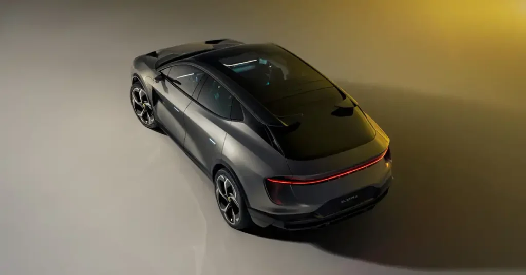 A high-angle shot shows the rear three-quarter view of a dark gray Lotus Eletre electric SUV. The car is positioned on a light gray surface with a gradient background that transitions from light gray on the left to a warm yellow-orange on the right.