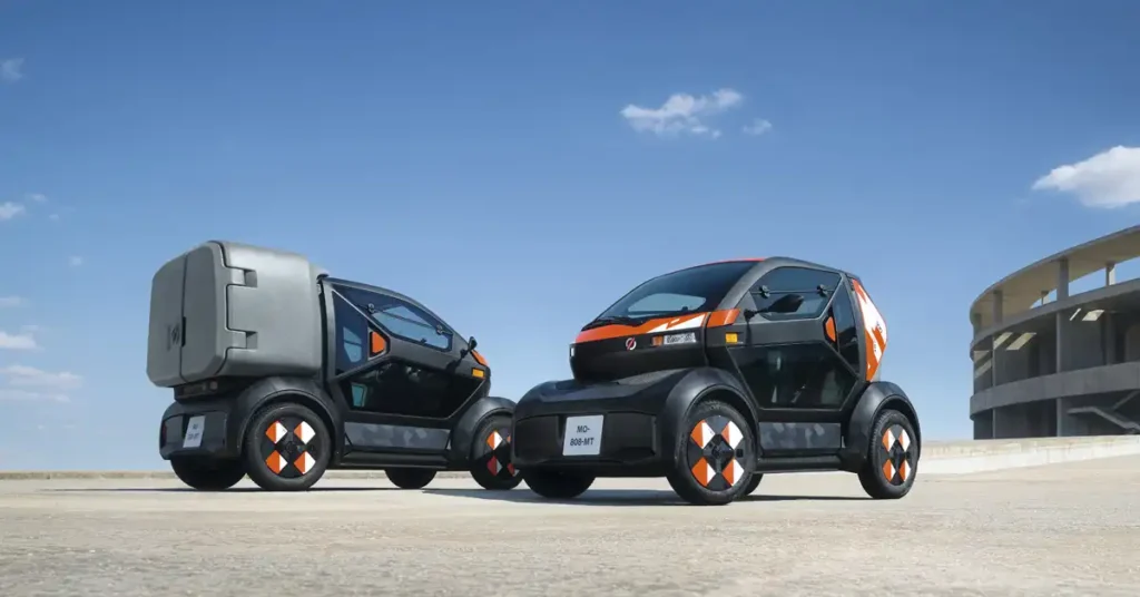 Two futuristic Renault Mobilize Duo & Bento, compact electric vehicles are parked on a concrete surface under a clear blue sky with a few wispy clouds.