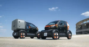 Two futuristic Renault Mobilize Duo & Bento, compact electric vehicles are parked on a concrete surface under a clear blue sky with a few wispy clouds.
