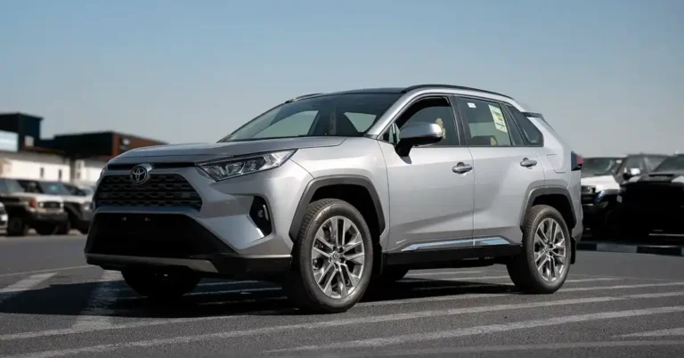 A silver Toyota RAV4 is parked on a paved lot with a clear blue sky above. The car is positioned at a slight angle, facing left, with its front end prominently displayed.