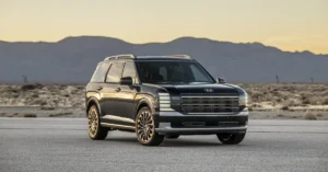A dark-colored 2026 Hyundai Palisade is parked on an asphalt road in a desert landscape. The SUV is positioned in the center of the frame, facing slightly to the left