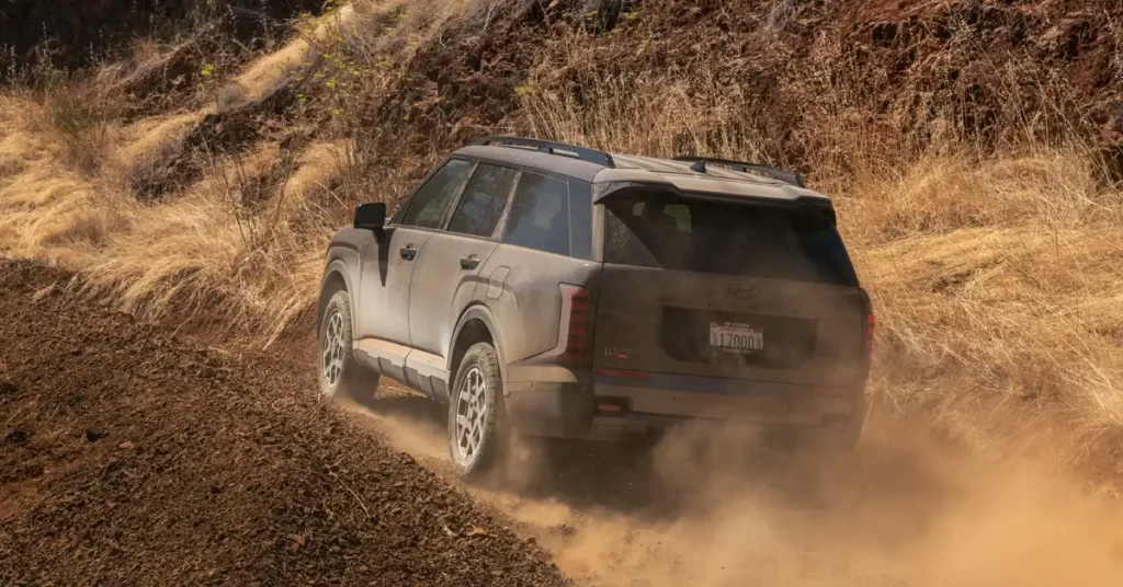 2026 Hyundai Palisade SUV The road is rough and uneven, with loose dirt and rocks. The surrounding landscape is dry and arid, with sparse vegetation.