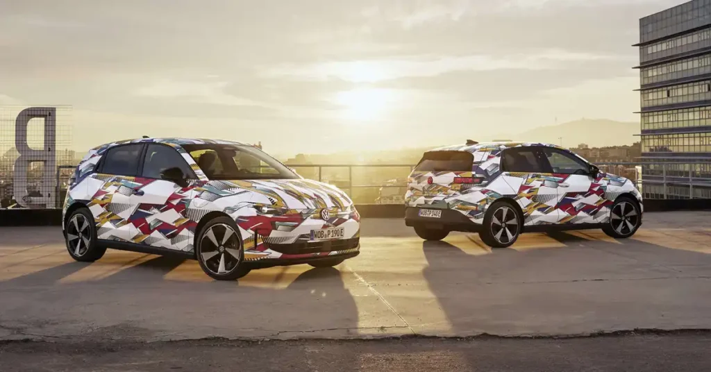 Two 2026 Volkswagen ID. Polo cars with a colorful geometric camouflage wrap are parked on a rooftop. The car in the foreground is angled towards the viewer, while the car in the background is seen from the rear.